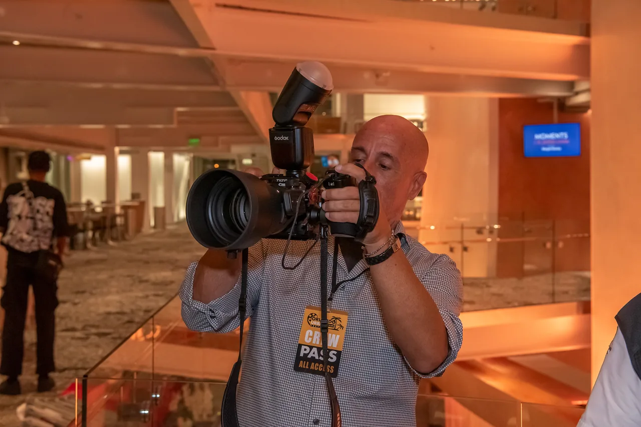 A festival photographer shooting with a flash-mounted camera, wearing a crew pass