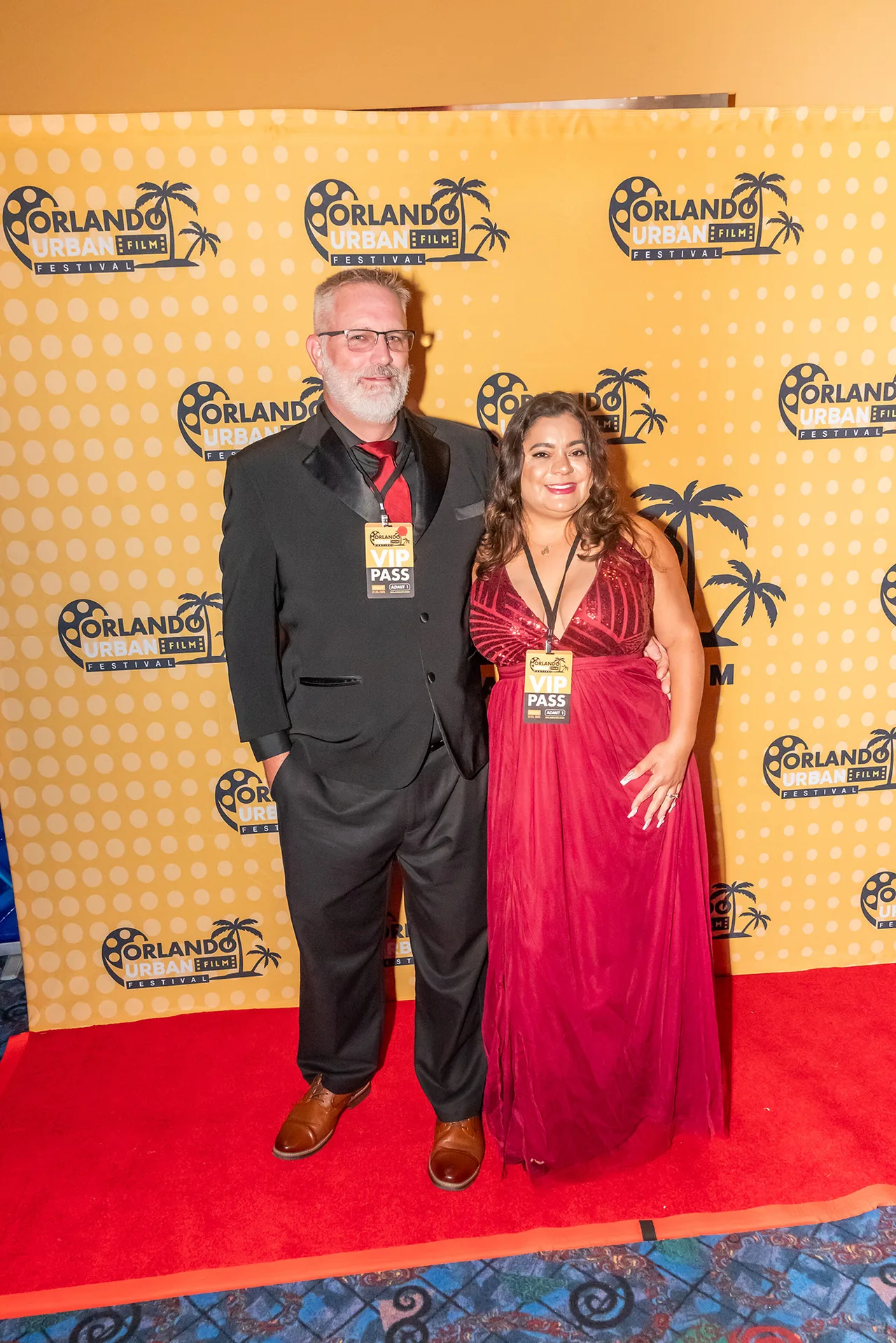 A couple on the red carpet, one in a dark suit and one in a red gown