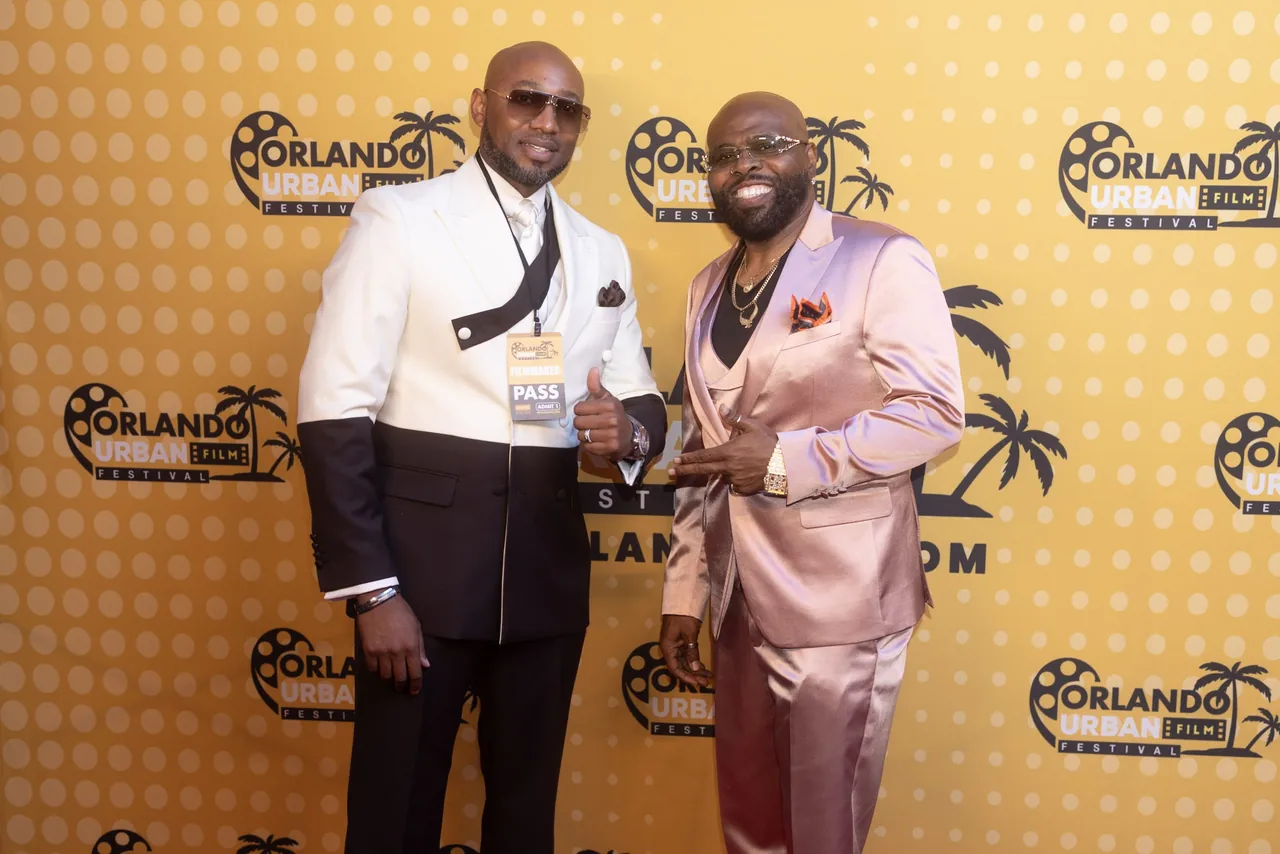 Two guests in white and pink suits posing together on the red carpet
