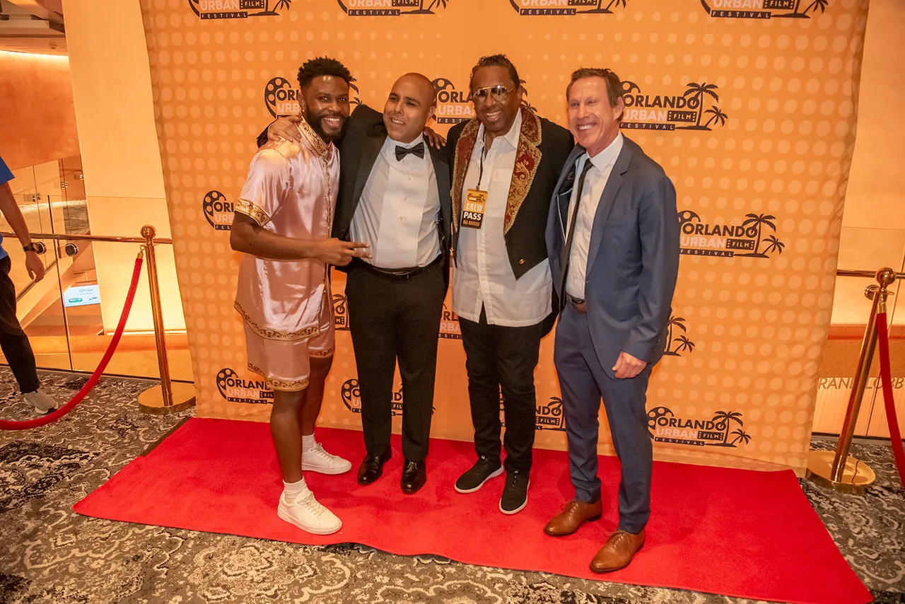Four men in suits posing shoulder to shoulder on the red carpet